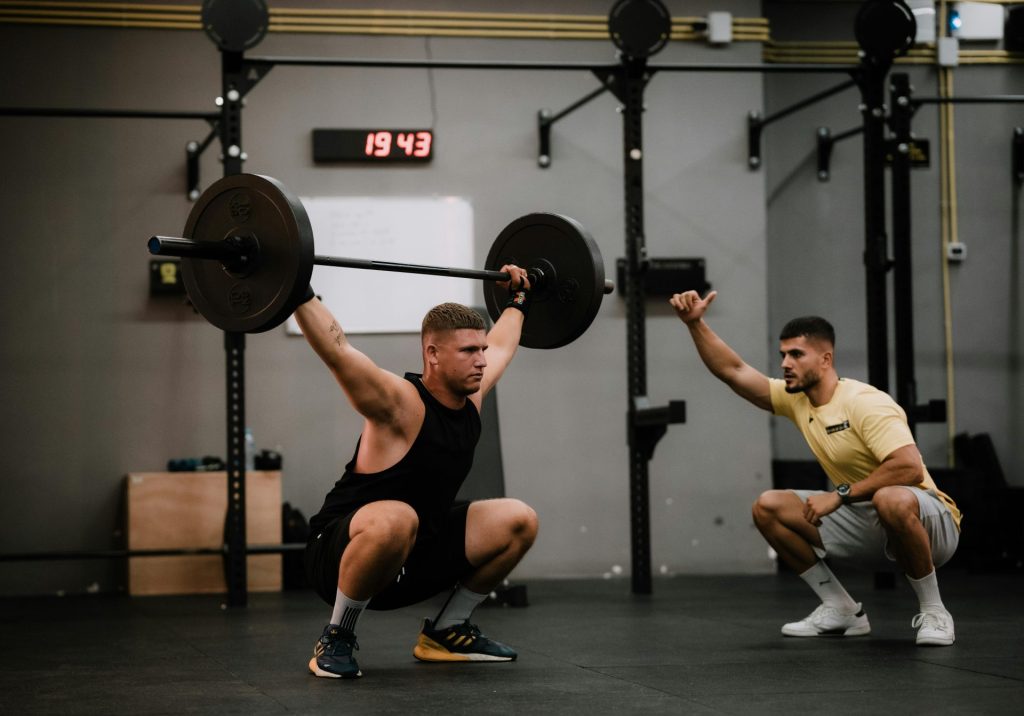A muscular man lifting a barbell with intense focus in a modern gym setting.