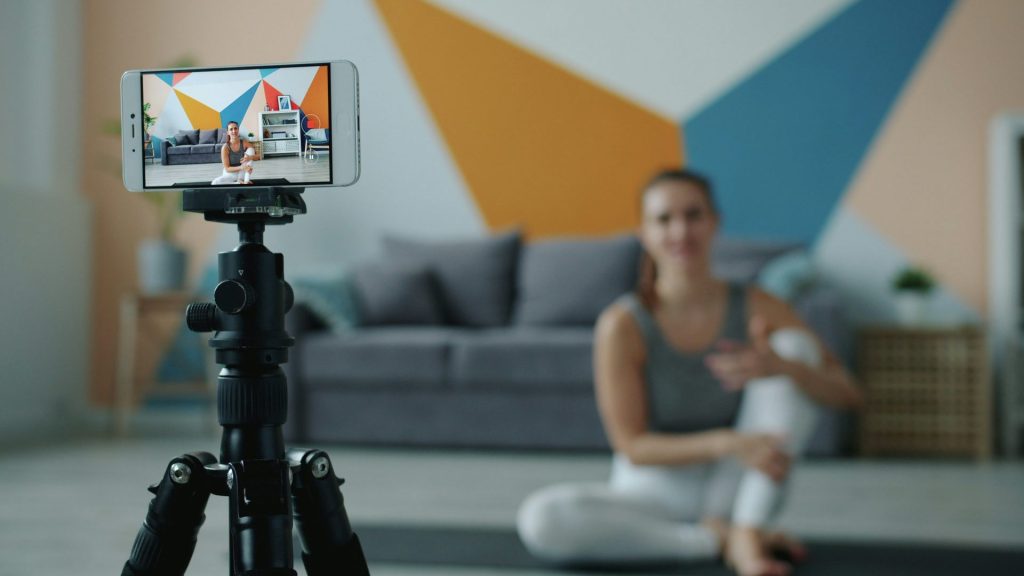 Woman recording fitness video on phone with tripod.